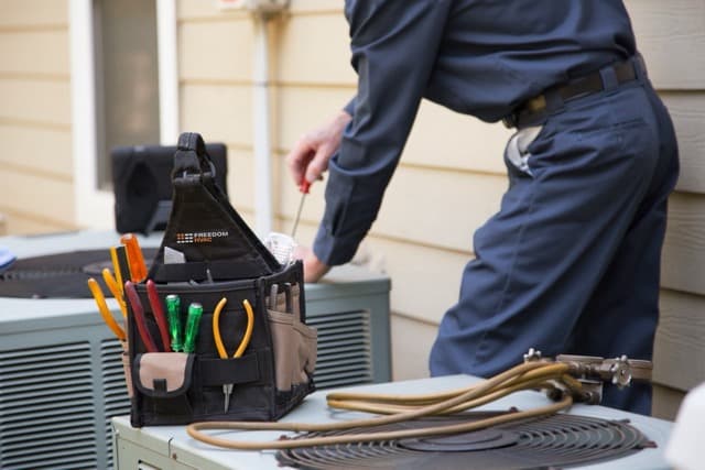 Service repair person adjusting an air conditioning unit with a tool