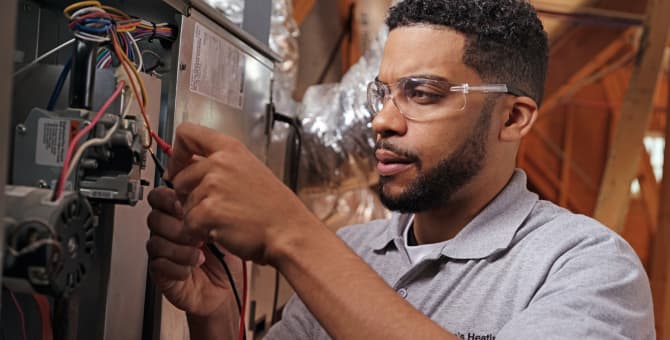 A service repair person wearing safety glasses taking a measurement with probes from a HVAC unit